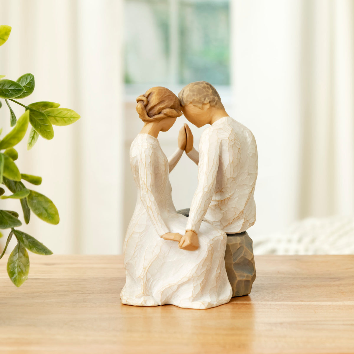 Willow Tree Around You, 6.5”h hand-painted figure of couple seated across from each other, heads and hands together, both in neutral clothing, on table near bright window