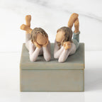 Front view of closed rectangular blue-gray resin box, sculpture of two girls affixed to lid