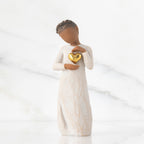 Front view: standing figure in cream dress with darker skin and dark hair braid, framing gold leaf heart with both hands on chest
