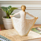 Willow Tree Butterfly, 6.5”h hand-painted standing resin figure in cream dress, holding sides of skirt out with hands, skirt has carved markings of a monarch butterfly with gold leaf, on desk with journal