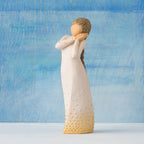 Front view, standing figure in cream dress, holding arms to face in wistful gesture. Hair and dress embellished with gold dots