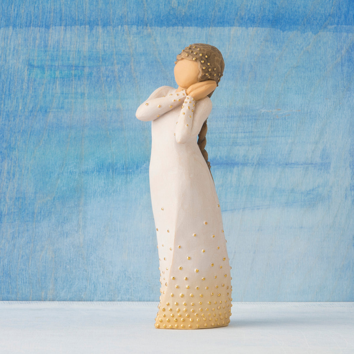 Front view, standing figure in cream dress, holding arms to face in wistful gesture. Hair and dress embellished with gold dots