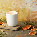 Willow Tree Festive Orange and Frankincense Candle, 3.5"h off-white ceramic vessel with plant-based wax and blend of natural oils, "behold the awe and wonder" sentiment in gold inside rim, in front of orange painting