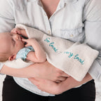 Close view of mother holding baby wrapped in cream towel that says 'so loved, so very loved' in blue