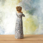 Willow Tree Music Speaks (lighter skin), back view of 7”h hand-painted standing resin figure wearing dress carved with symbols of music and dancing, in front of blue-green painting