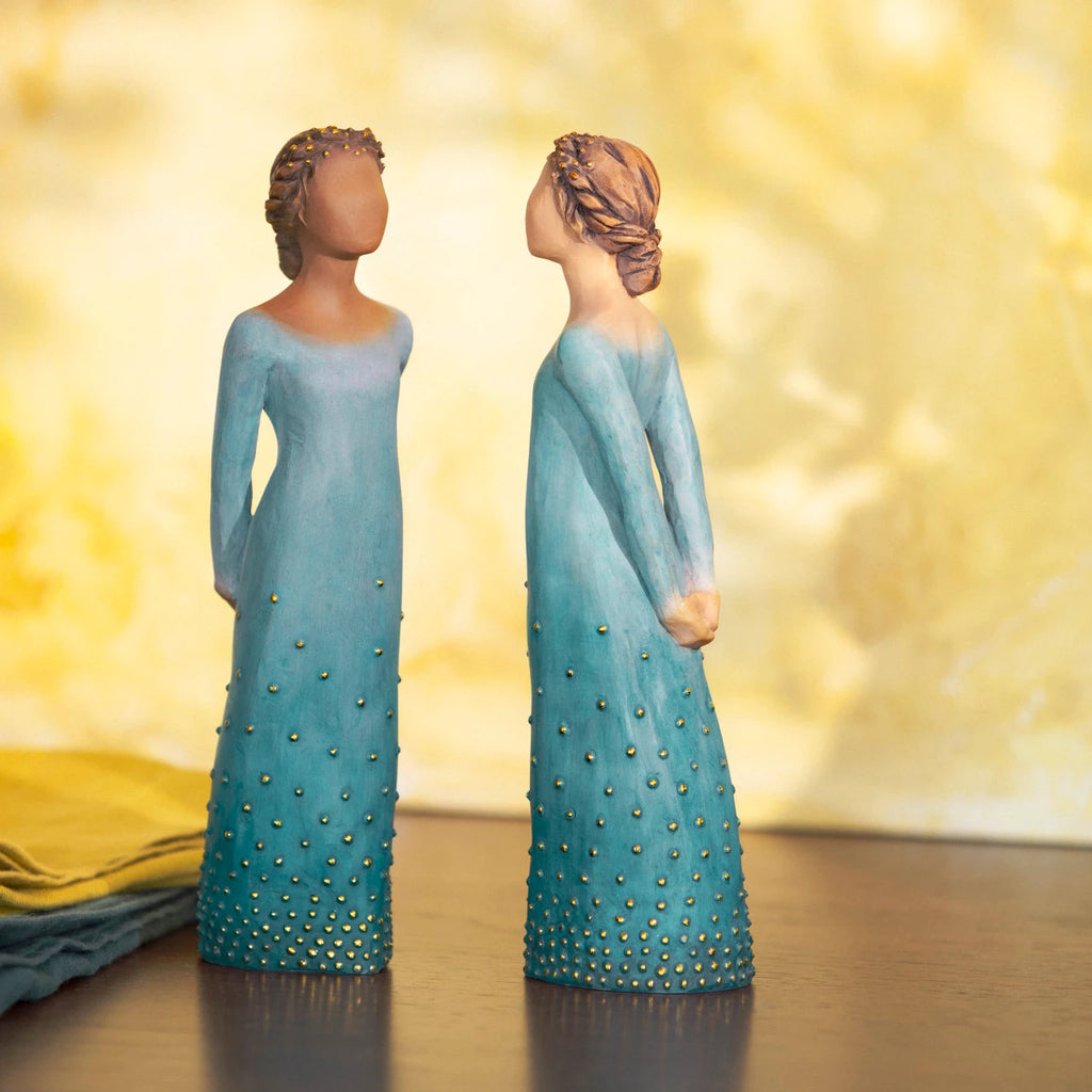 Willow Tree Radiance, back view of 7.5”h hand-painted standing resin figure with lighter skin and hair, in deep blue ombré dress dotted with gold leaf, arms clasped behind back, on wooden table
